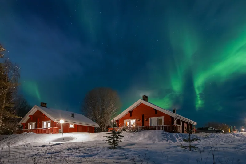 Chalets rouges et neige sous une aurore boréale en Finlande