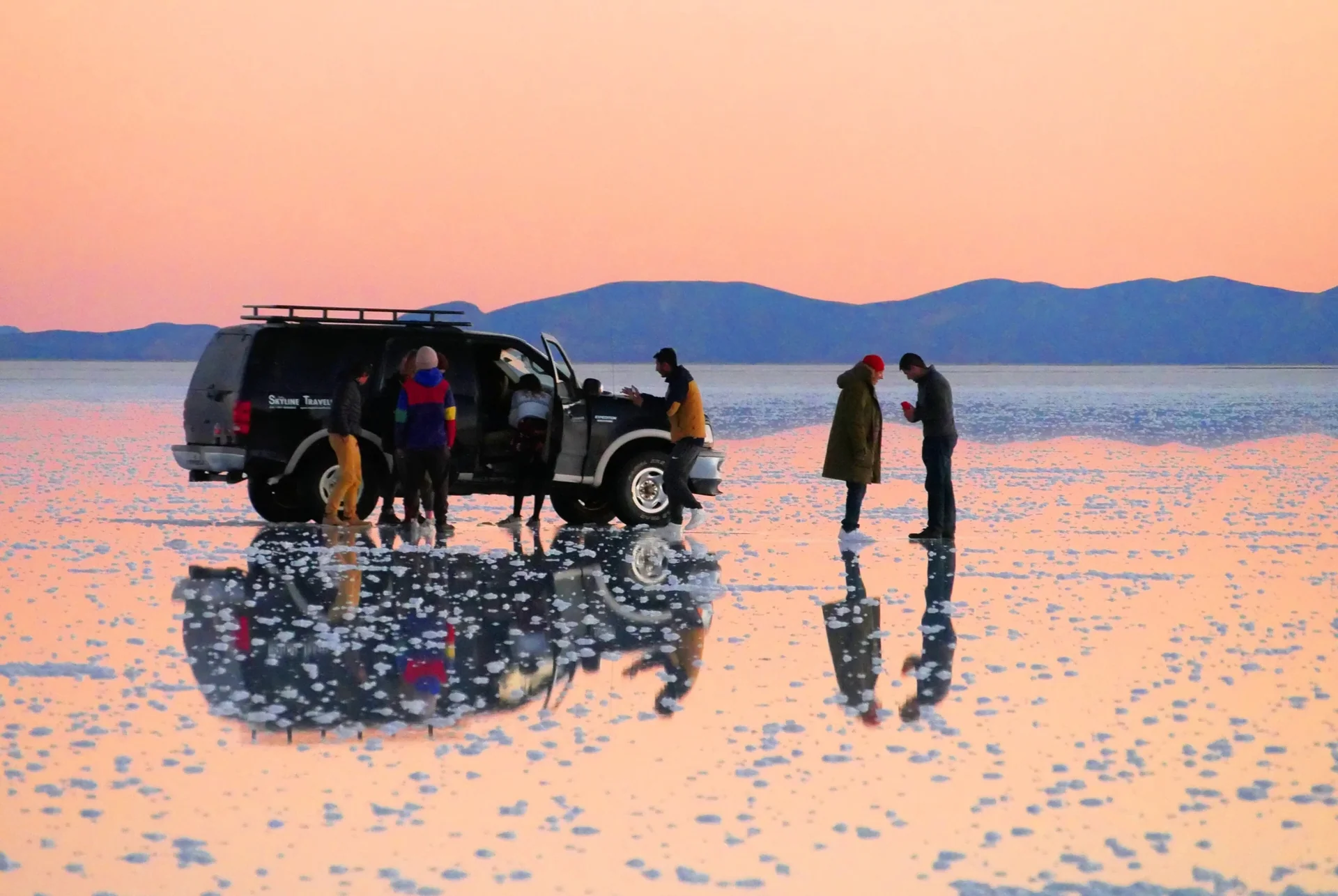 Voyageurs et véhicule se reflétant sur le Salar d’Uyuni